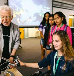 A participant handles a robotic remote while a researcher and other participants look on.